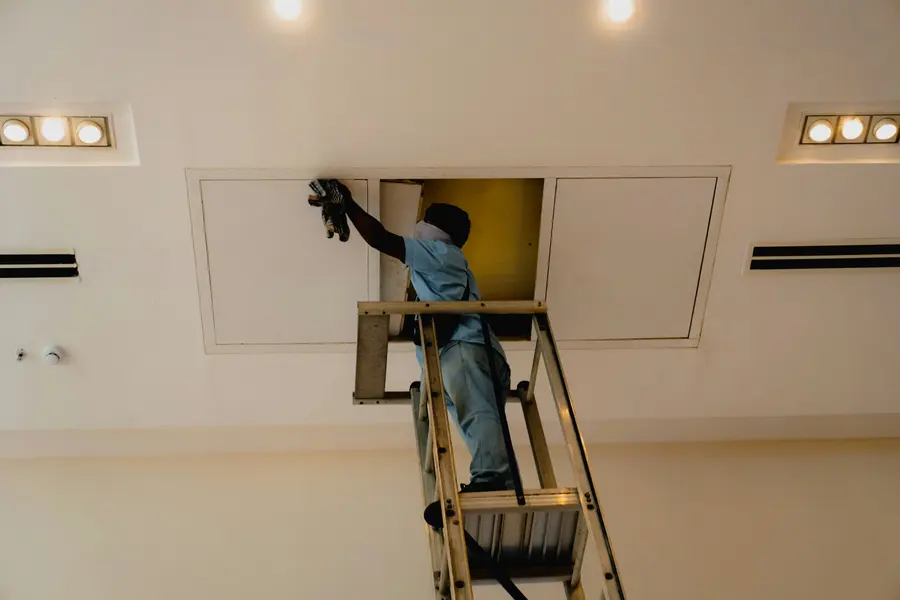 Profissional na escada abrindo o alçapão do forro